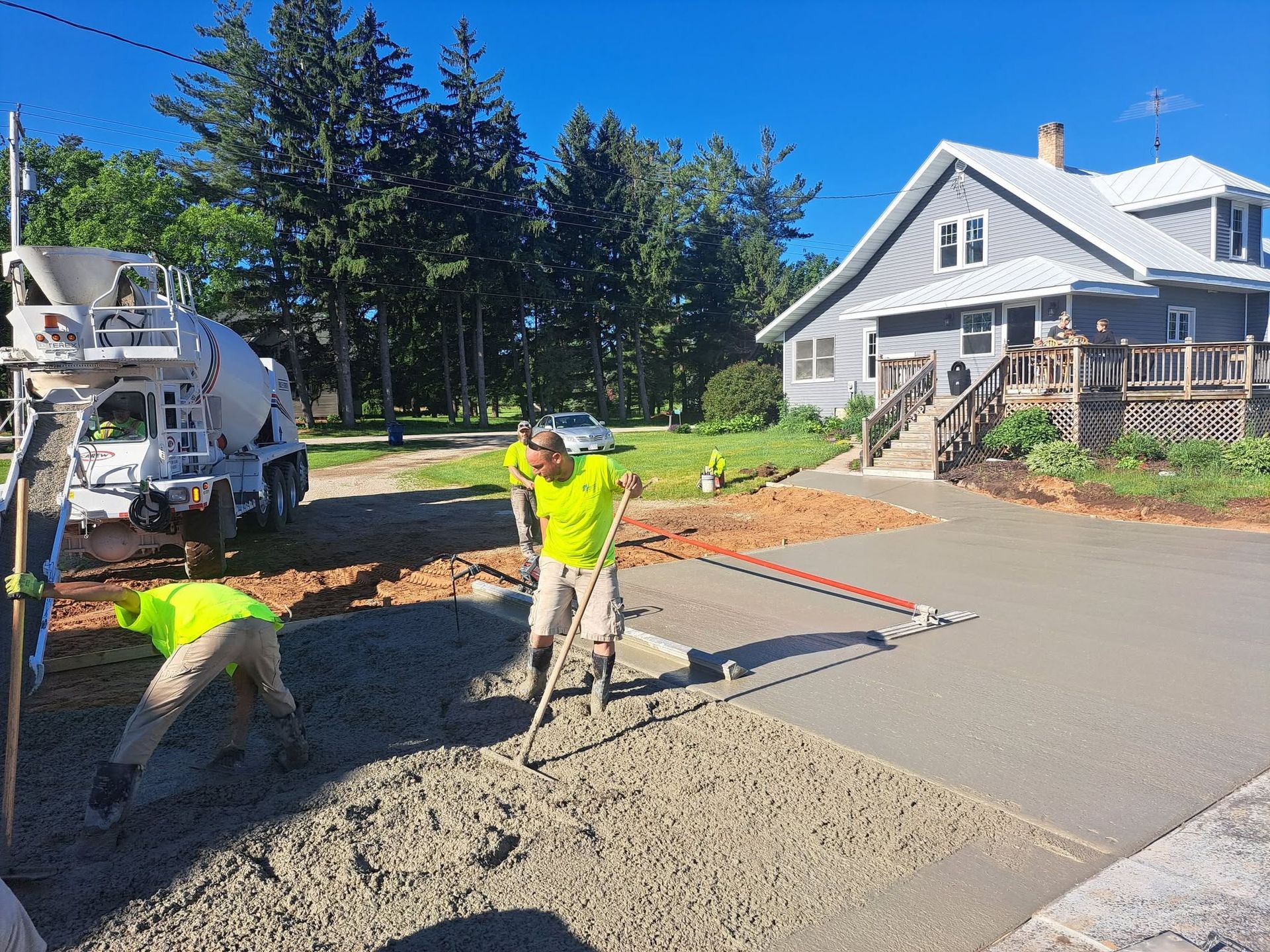 Workers paving a driveway beside a white house, with a cement mixer truck and wet concrete.