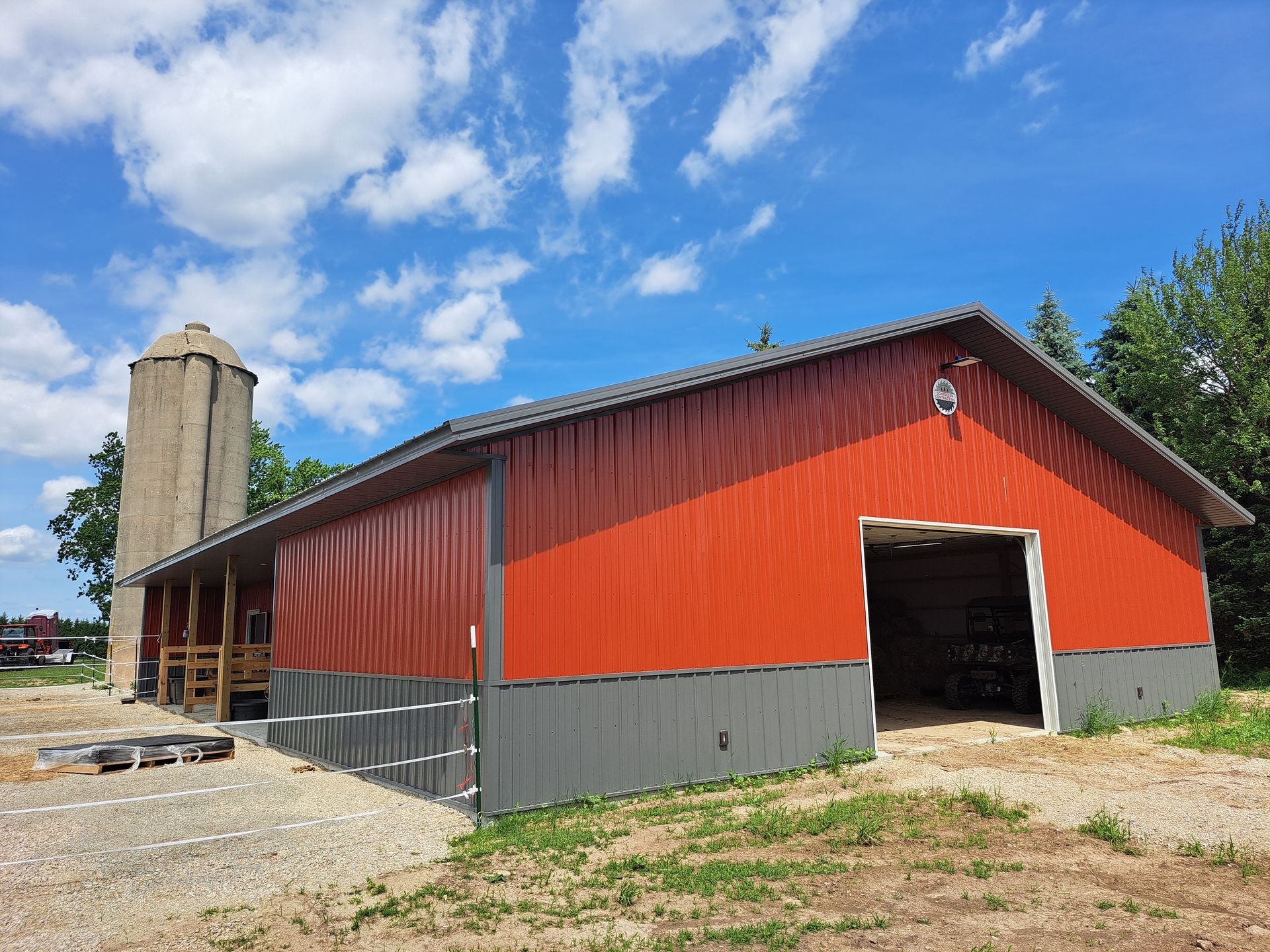 Red barn with open doorway beside a tall silo under a blue sky with clouds