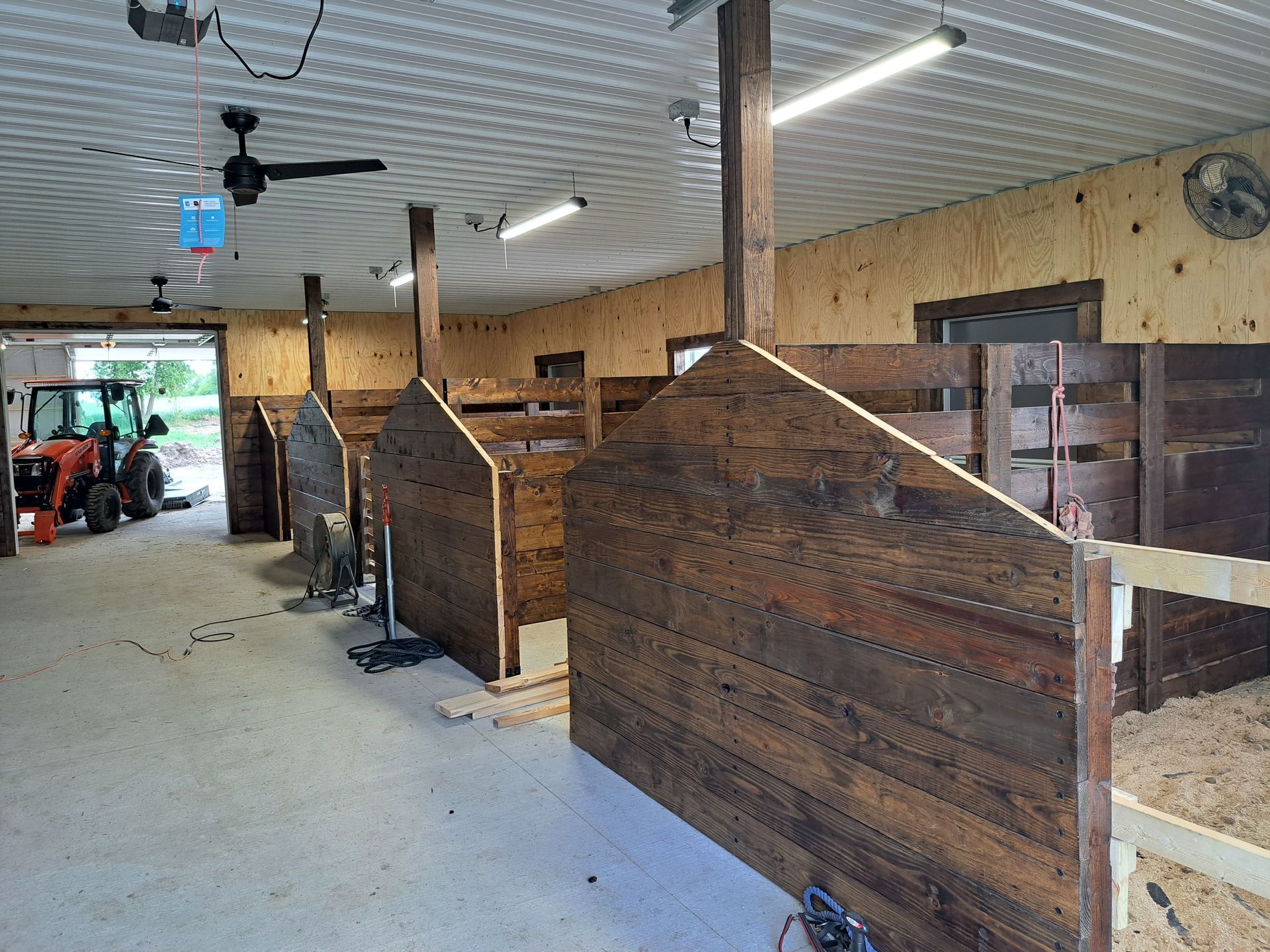 Indoor stable aisle with wooden horse stalls and a horse visible in the left background