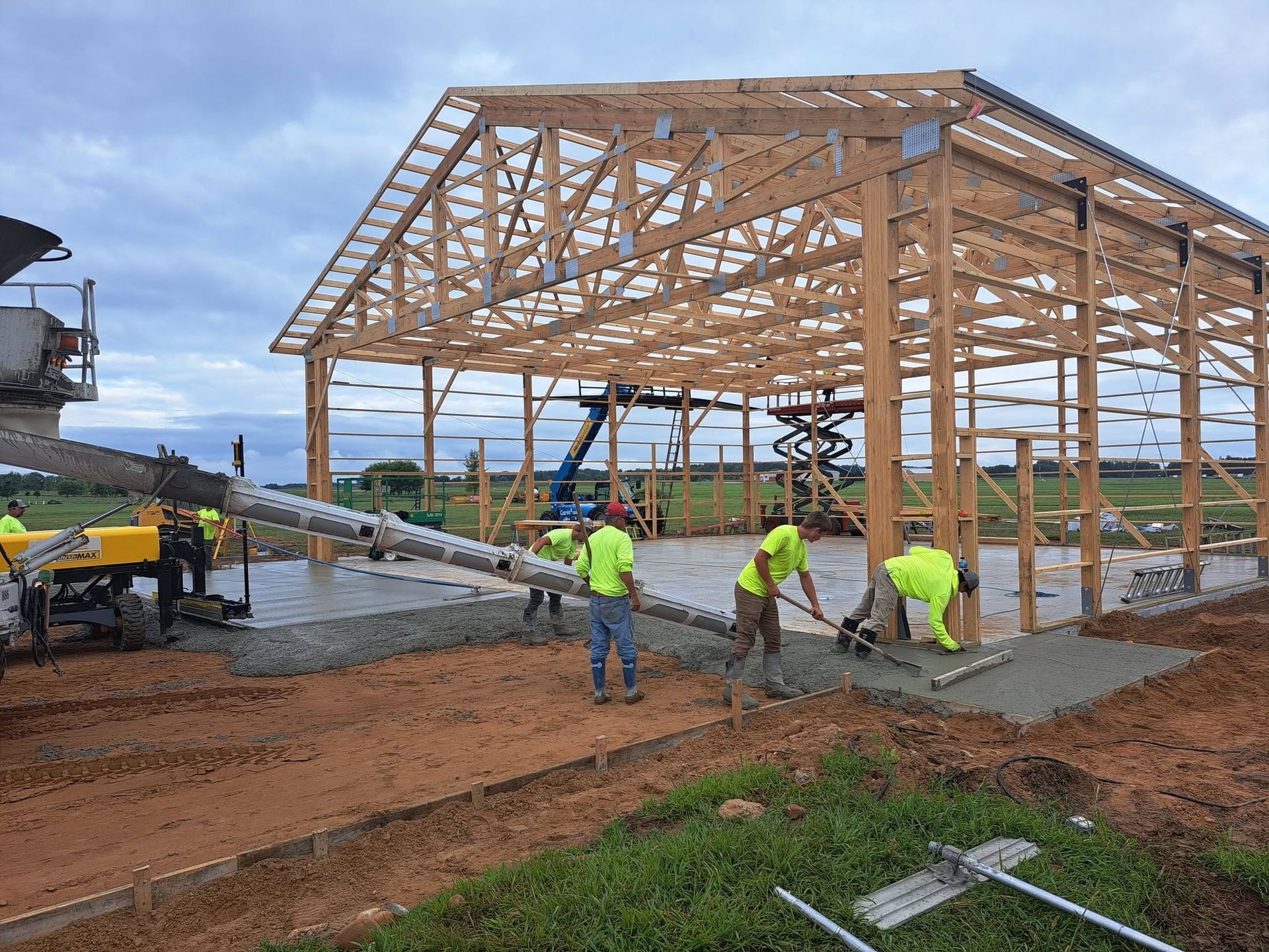 Workers pour concrete at a large wooden building frame on a construction site.