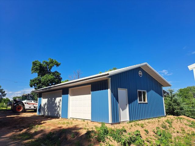 Blue and white metal garage with roll-up door on a dirt lot under a clear blue sky