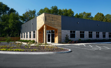 A large building with a wooden facade and a metal roof is sitting next to a parking lot