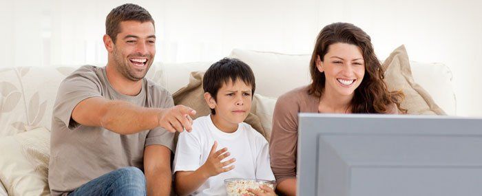 A family is sitting on a couch watching television 