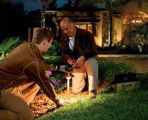 Two men are kneeling in the grass in front of a house at night