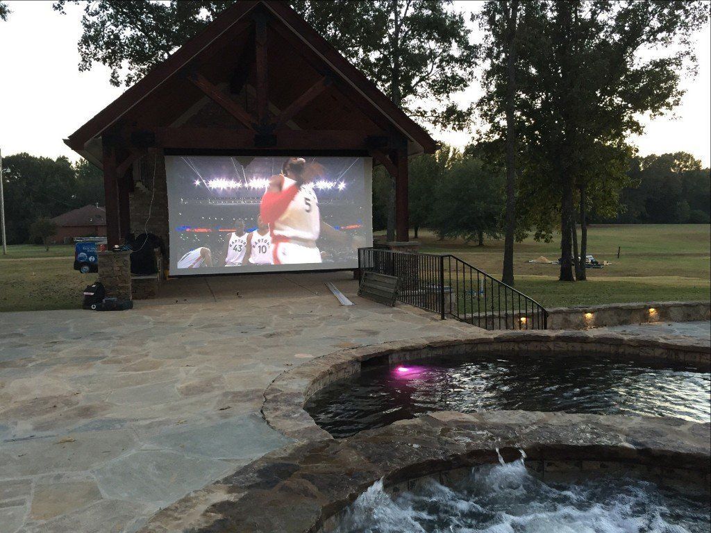 A large screen is projected on the side of a building next to a pool