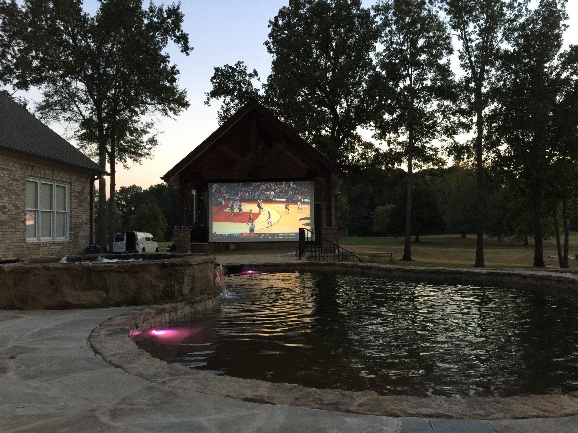 A large screen shows a basketball game in front of a pond