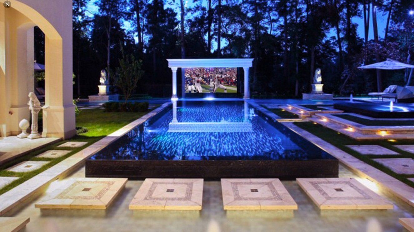 A large swimming pool is surrounded by trees at night