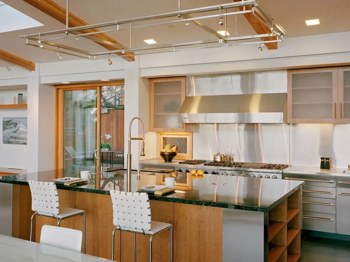 Modern kitchen with island, wood cabinets, stainless hood, bar stools, and bright natural light