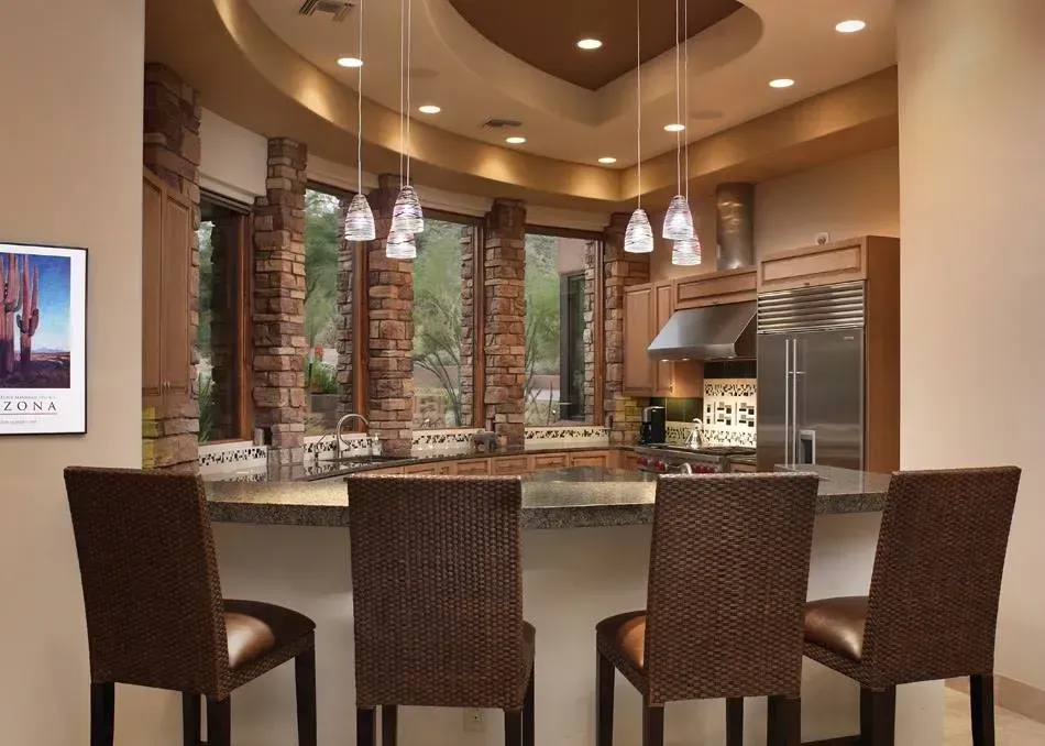 Modern kitchen with curved island, pendant lights, and four bar stools in a warm tan interior