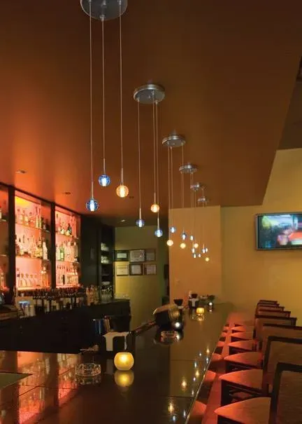 Dimly lit modern bar interior with pendant lights, glossy counter, and rows of stools and tables