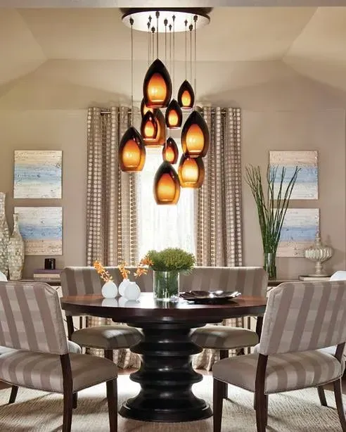 Modern dining room with a dark round table, striped chairs, and warm teardrop pendant lights.