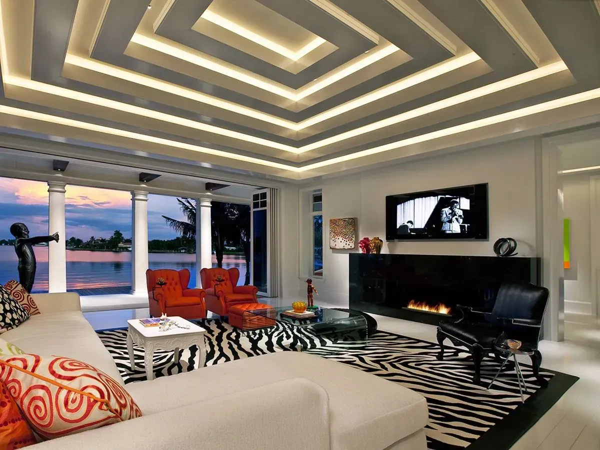 Modern living room with recessed ceiling lights, zebra rug, black sofas, and ocean view at sunset