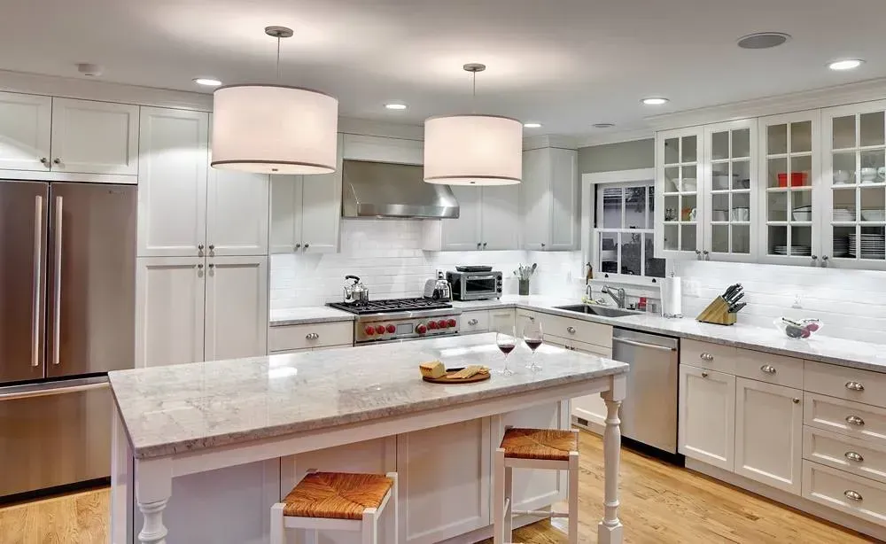 Bright modern kitchen with white cabinets, marble island, stainless fridge, and pendant lights