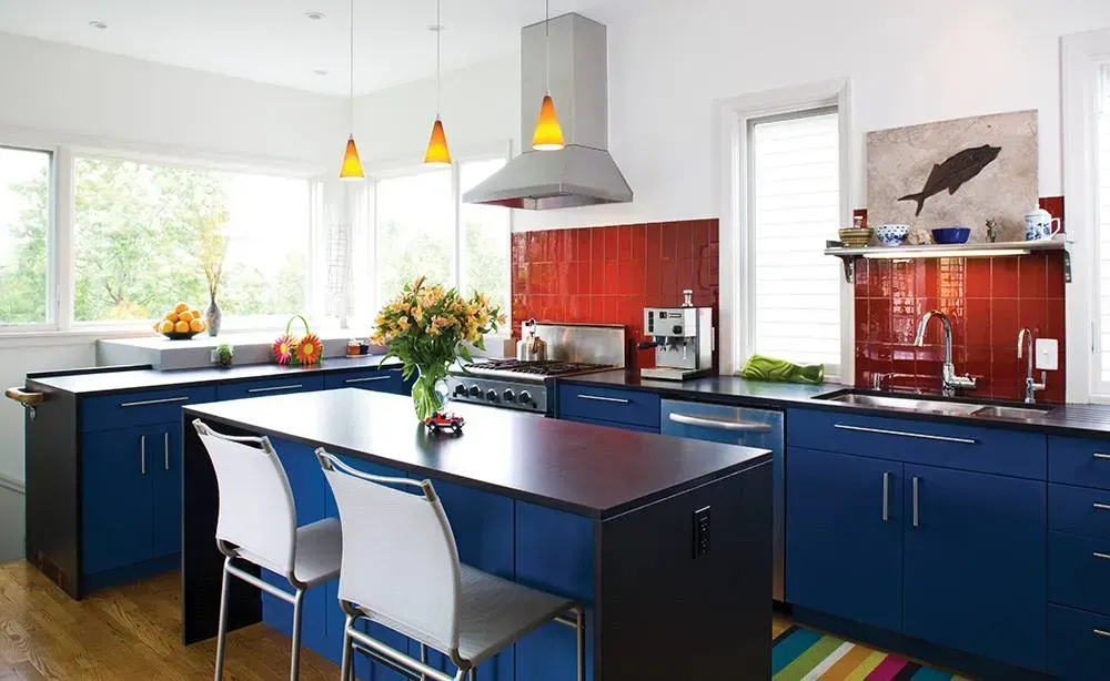 Modern kitchen with blue island, red backsplash, pendant lights, and large windows