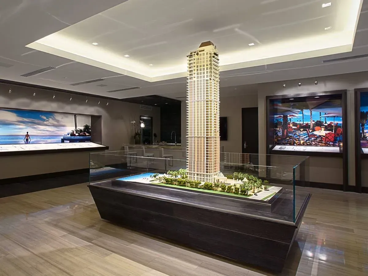 Modern lobby with a tall illuminated tower model in a black display planter and wall screens in the background