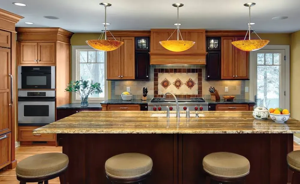 Modern kitchen with large granite island, wood cabinets, stainless appliances, pendant lights, and bar stools