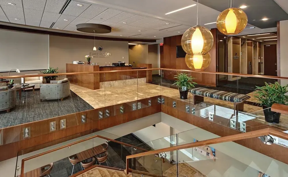 Modern office atrium with wood walkways, glass railings, and warm hanging lights