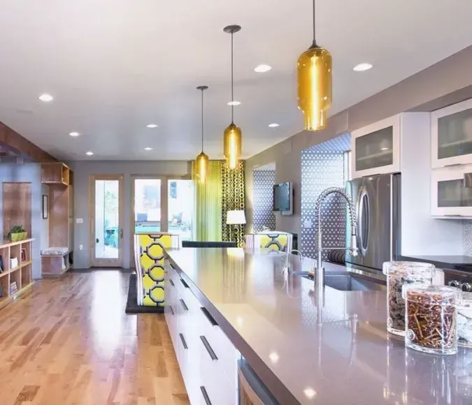 Modern kitchen with white island, stainless sink, yellow pendant lights, and hardwood floors
