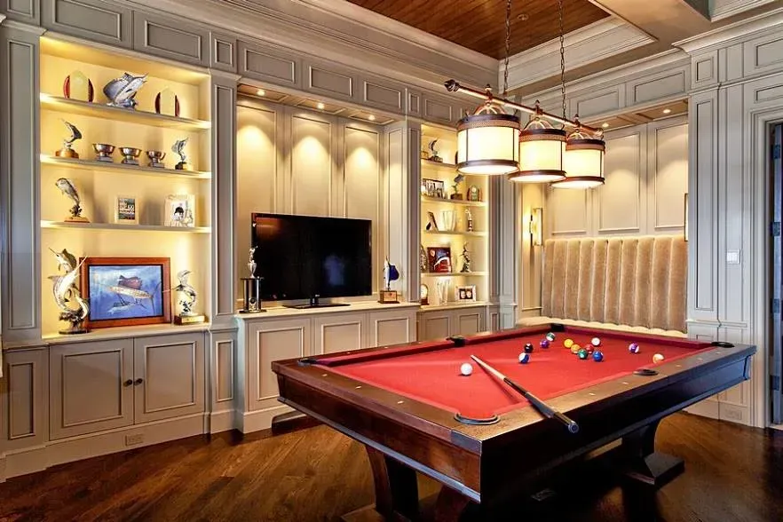 Elegant game room with a billiards table, built-in shelving, and a wall-mounted TV under warm lighting