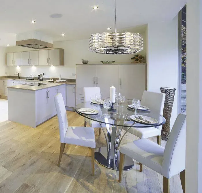 Modern open-plan kitchen and dining area with glass table, white chairs, and a silver chandelier