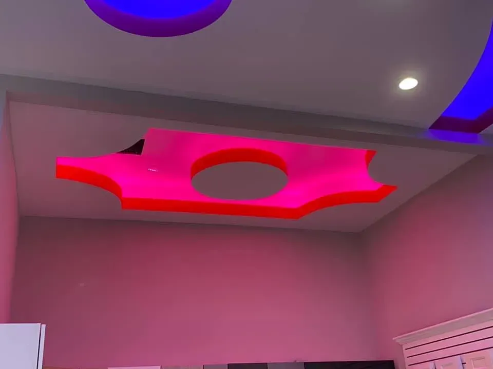 Ceiling with a glowing red geometric light fixture in a pink room, with blue accent lights above.