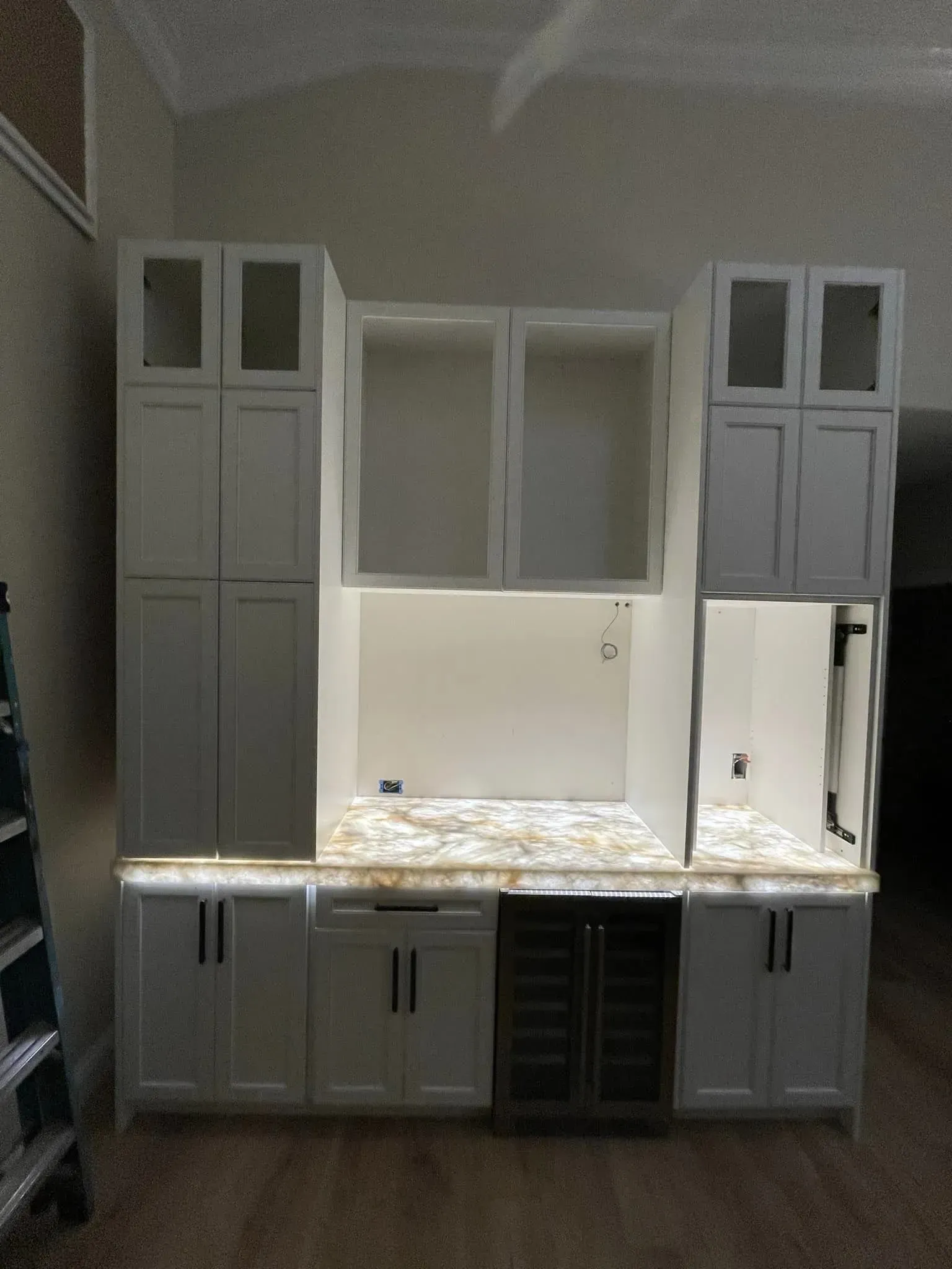 White built-in kitchen cabinets with a marble countertop and central window against a plain wall.