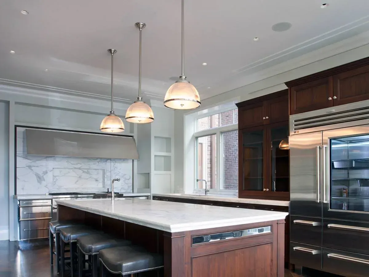 Modern kitchen with large island, pendant lights, marble backsplash, and stainless steel appliances