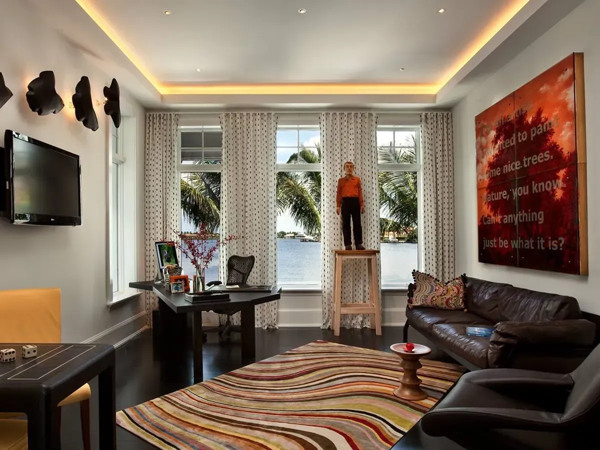 Modern living room with leather sofas, colorful rug, wall art, and large windows overlooking greenery