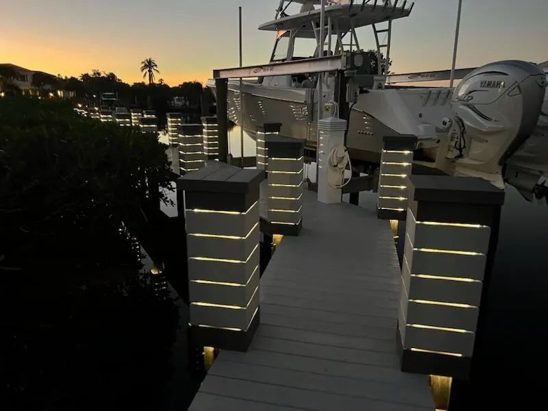 Lit dock walkway with illuminated posts beside moored boats at dusk