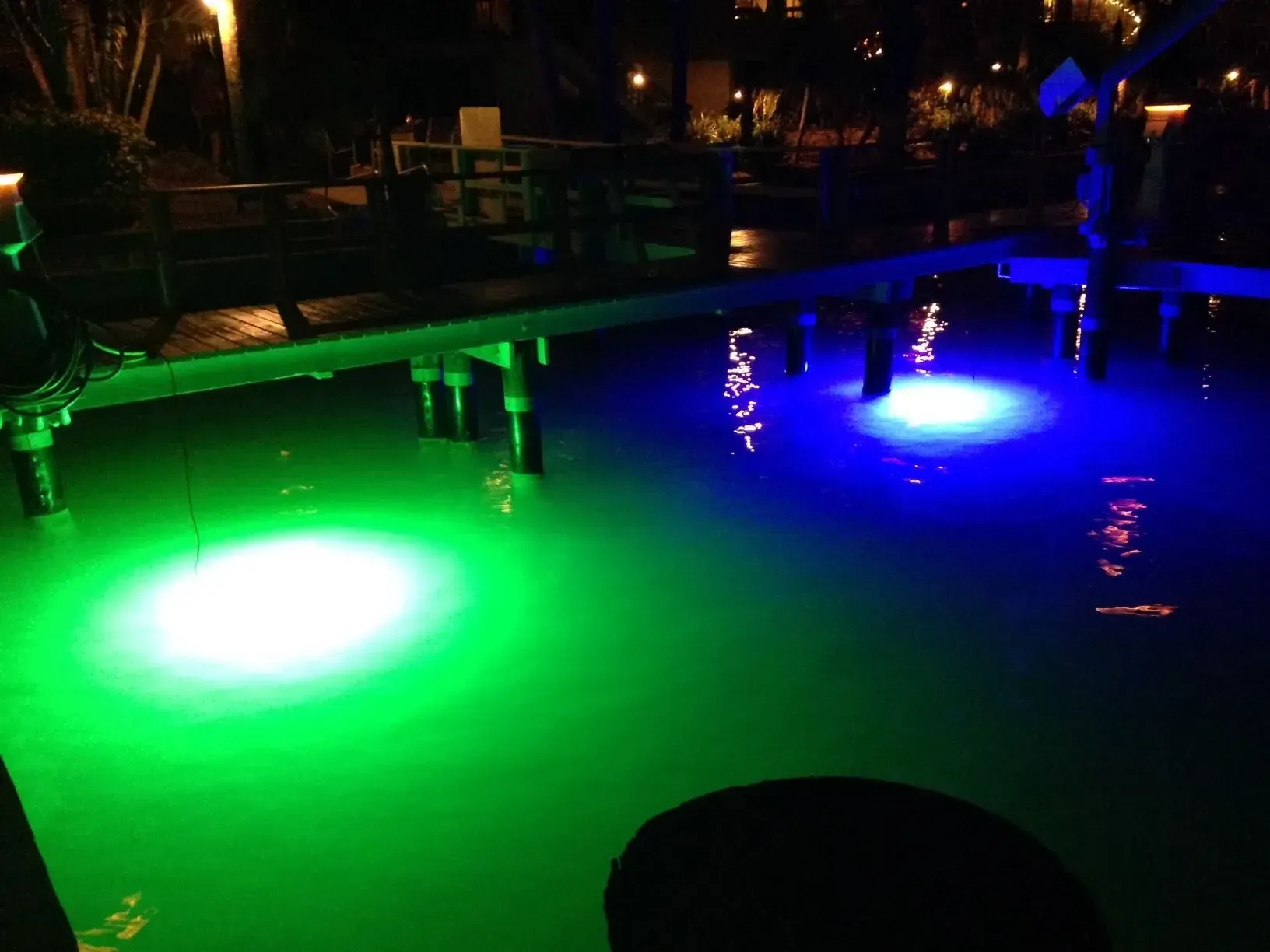 Colorful illuminated pool at night with green and blue underwater lights under a table