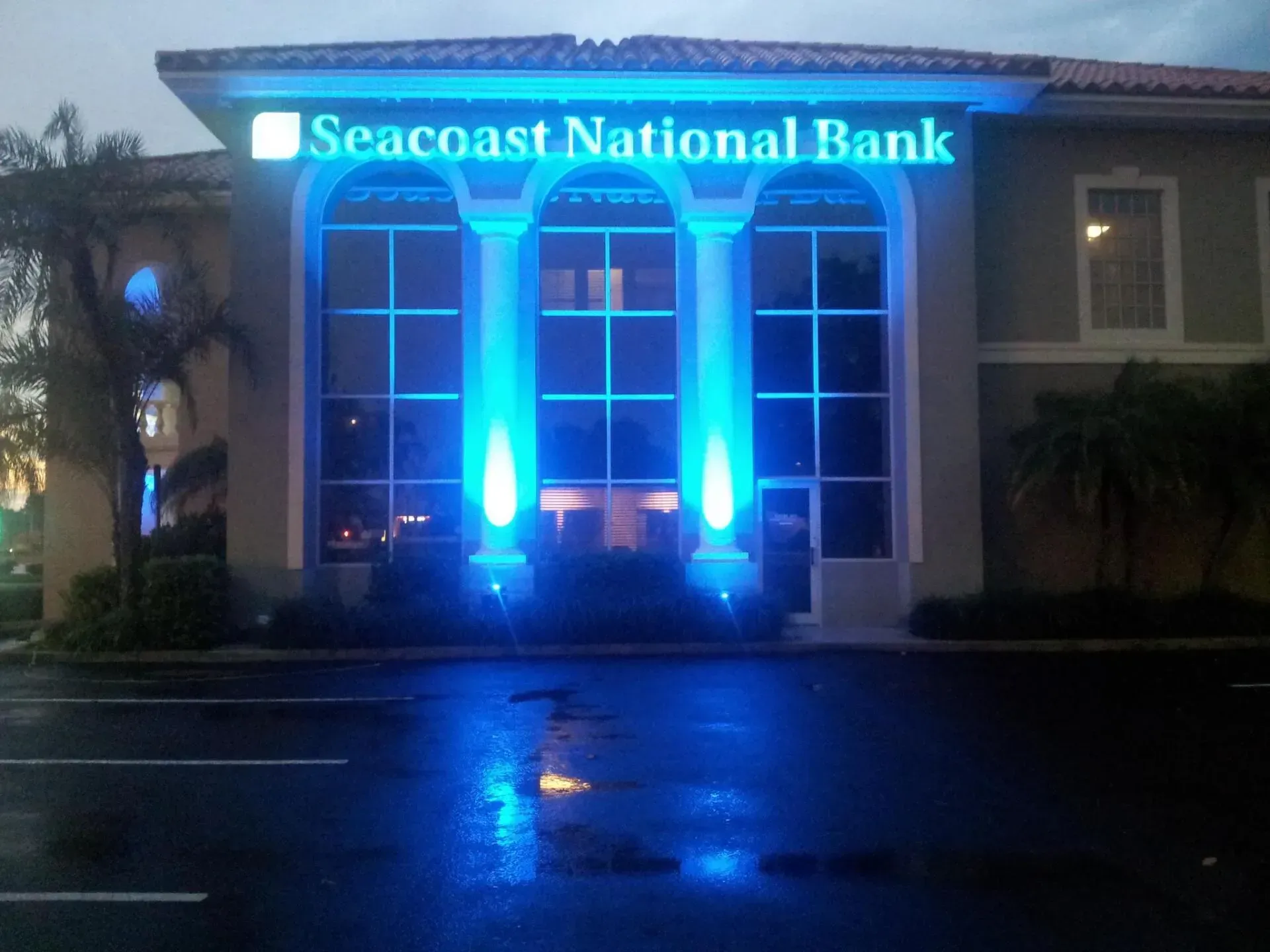 Seacoast National Bank building at night, lit with bright blue lights and wet pavement in front