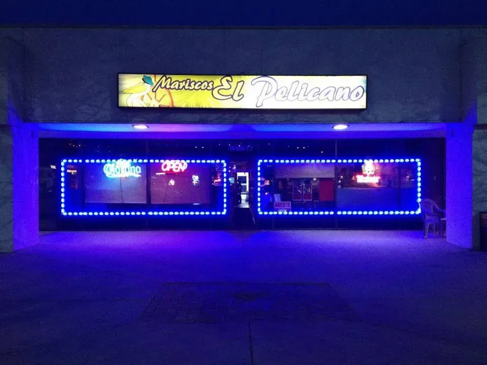 Blue-lit storefront at night with a sign reading “El Pelicano” above large windows