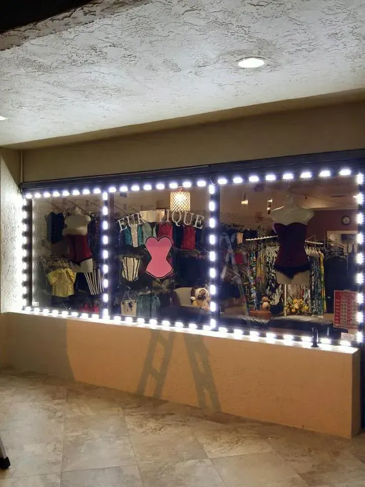 Lit vanity mirror with bright bulbs and colorful clothes reflected in a room or salon