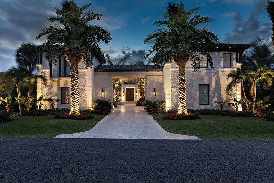 Luxurious two-story house at dusk with lit palm trees and a central walkway leading to the front entrance