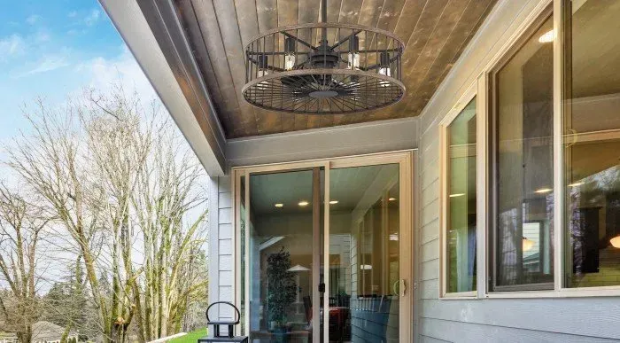 Covered porch with ceiling fan, glass door, and large windows overlooking trees