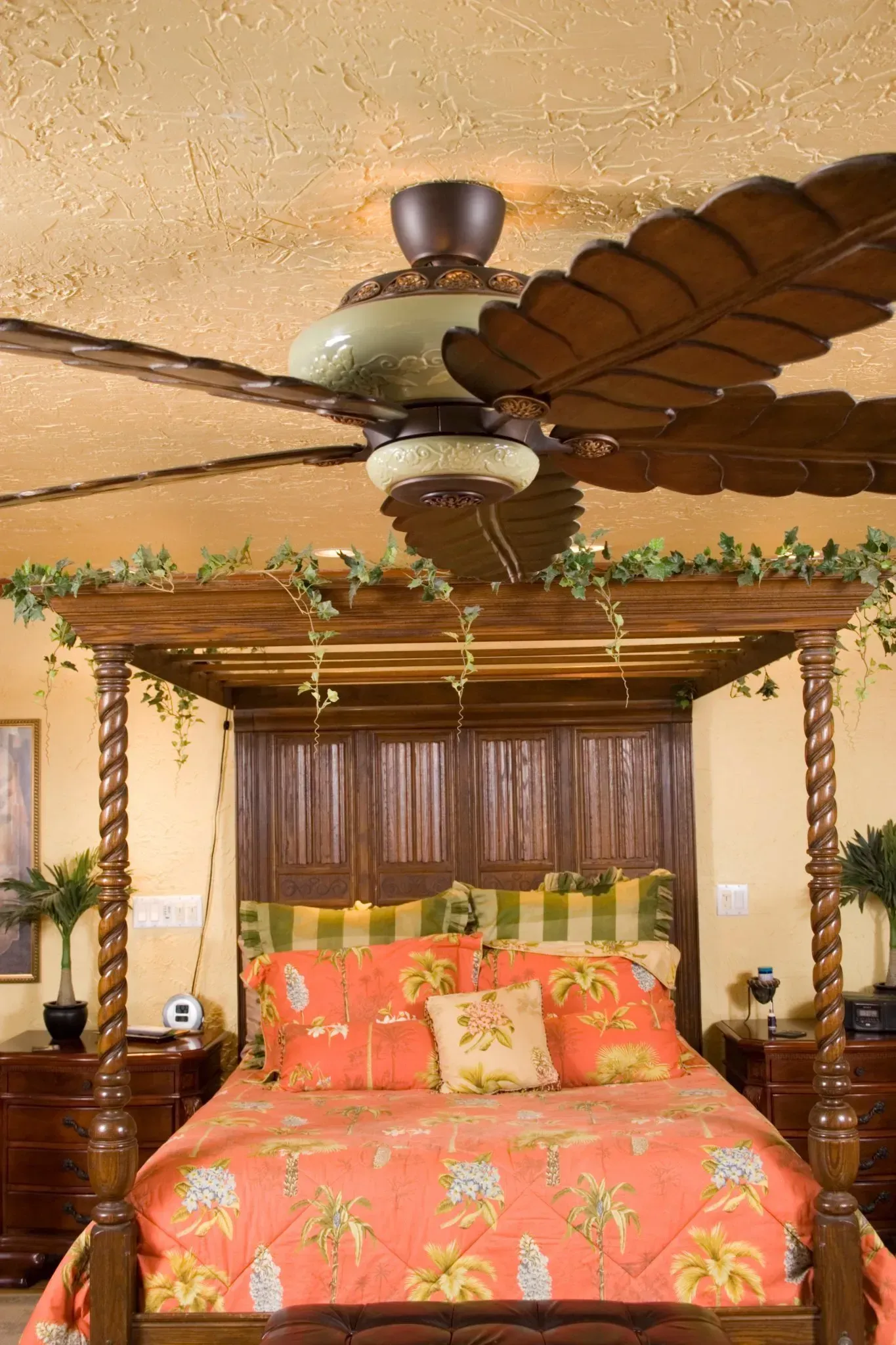 Four-poster bed with coral floral bedding in a cozy bedroom, under a ceiling fan and wooden canopy