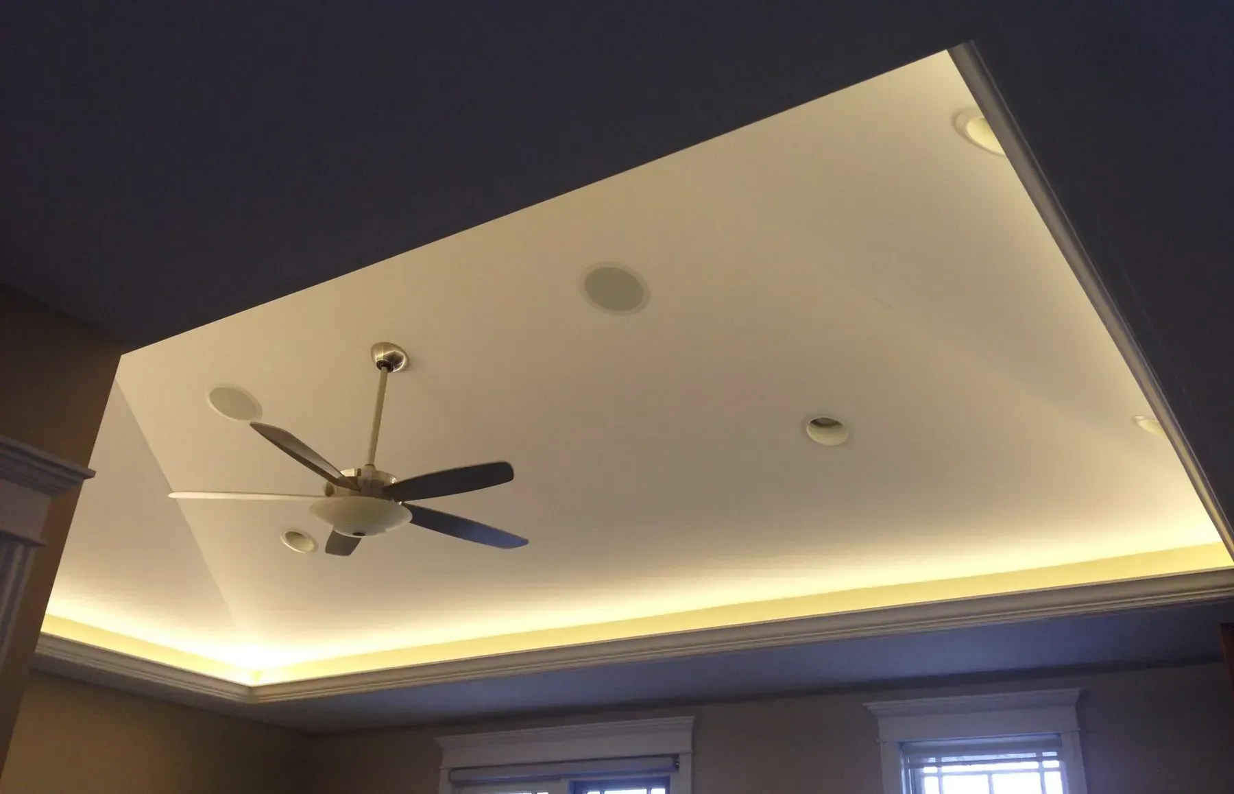 Ceiling with recessed lighting, a ceiling fan, and soft cove light in a modern room.
