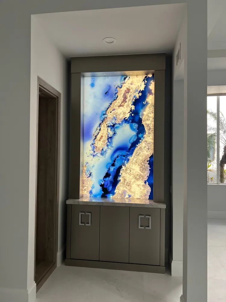 Backlit abstract blue and gold artwork mounted in a hallway alcove above a cabinet
