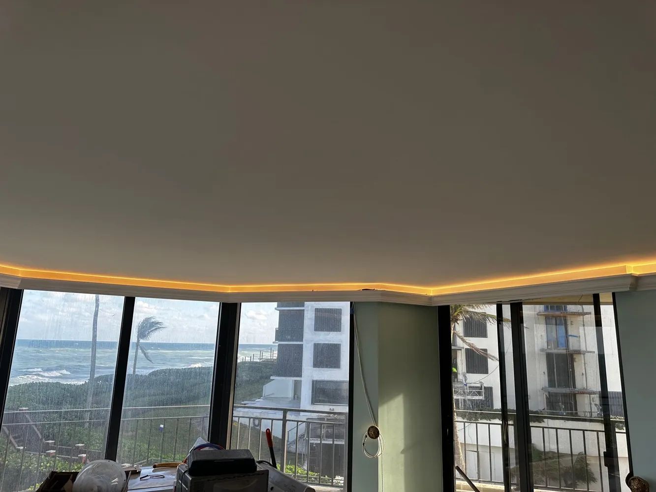 Modern room with floor-to-ceiling windows, city view, and warm cove ceiling lighting