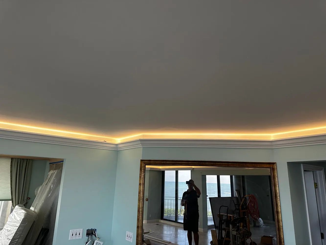 Living room with cove ceiling lights, curtains, a large mirror, and a person standing near the window