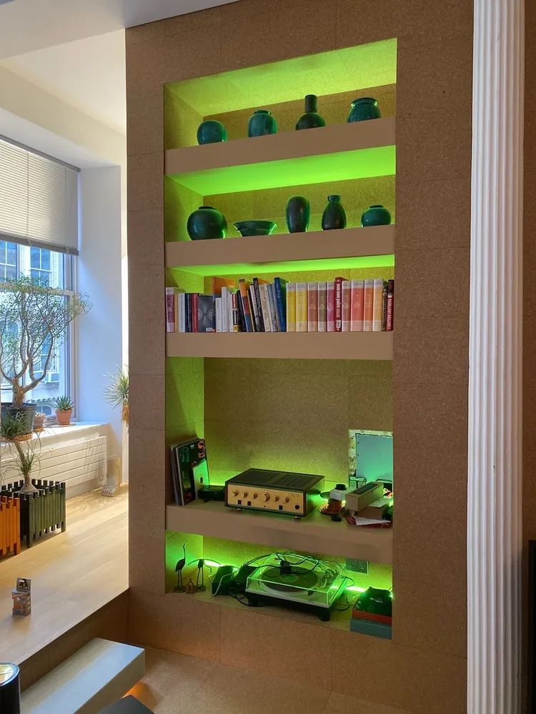 Wall shelf with green LED-lit displays, books, and small decor in a modern room nook