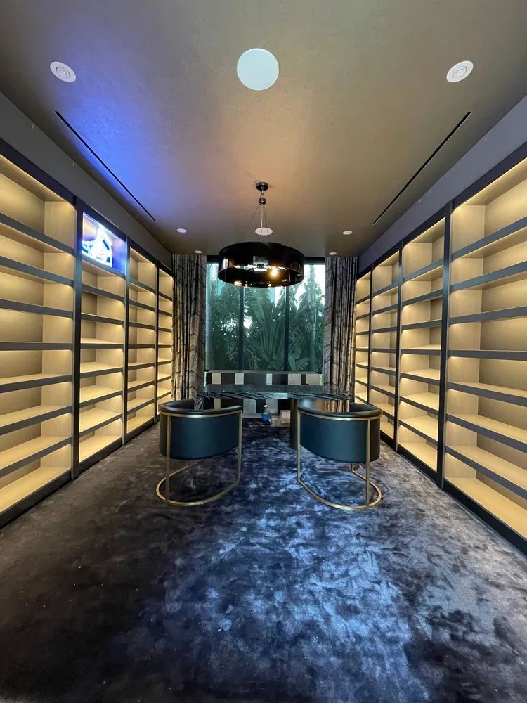 Modern boutique showroom with shelving, blue carpet, and a central black table under warm ceiling lights
