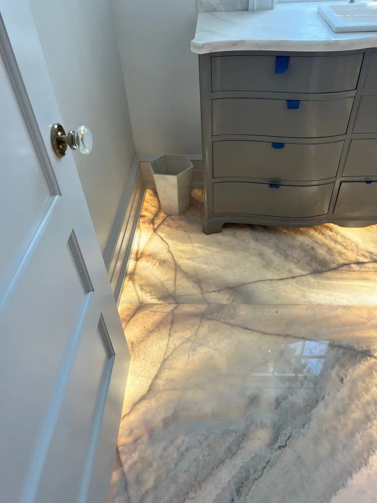 Sunlit bedroom corner with white door, marble floor, and gray dresser with drawers.