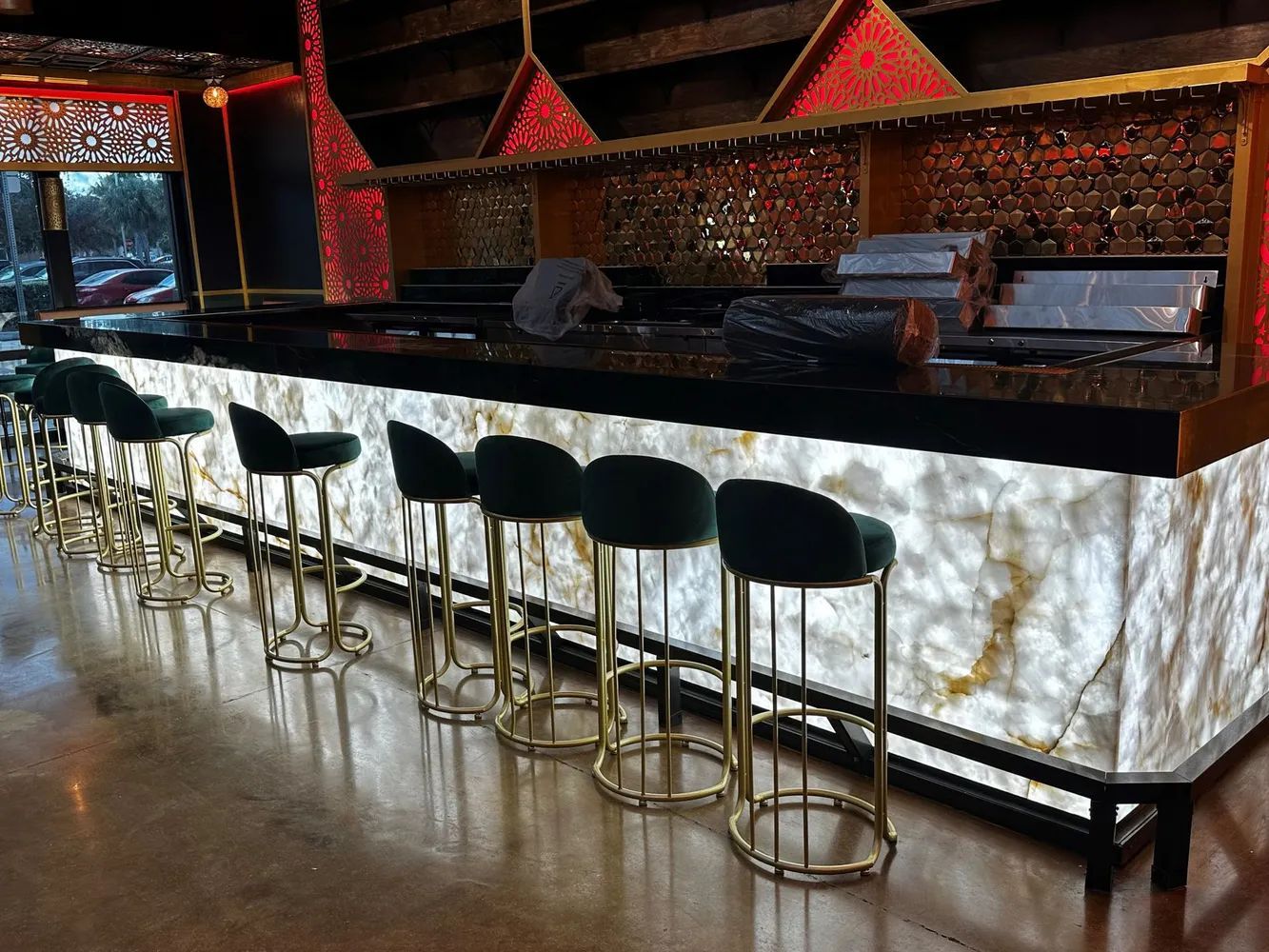 Empty bar with black stools, glossy black counter, and glowing marble front in a dim lounge.