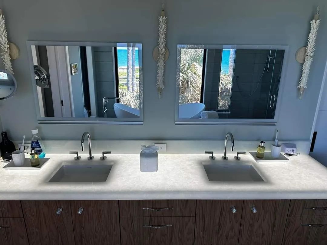 Modern bathroom vanity with double sinks, mirrors, and toiletries on a light countertop.