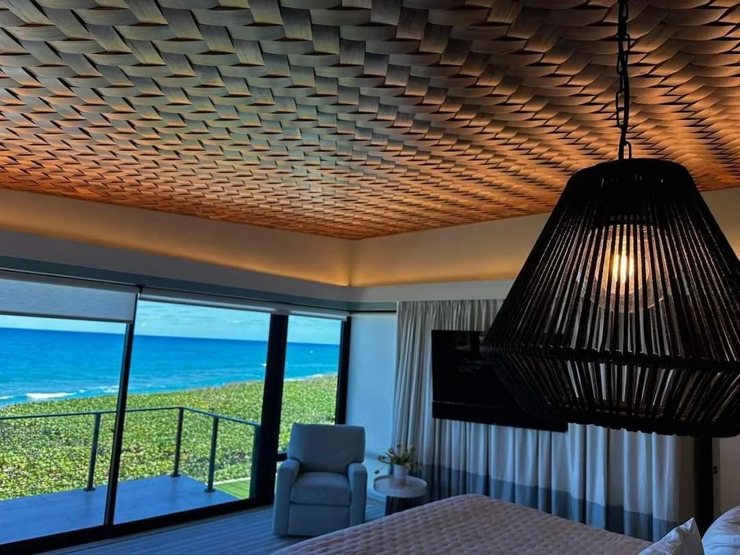 Ocean-view living room with large windows, patterned wood ceiling, and a hanging black pendant lamp