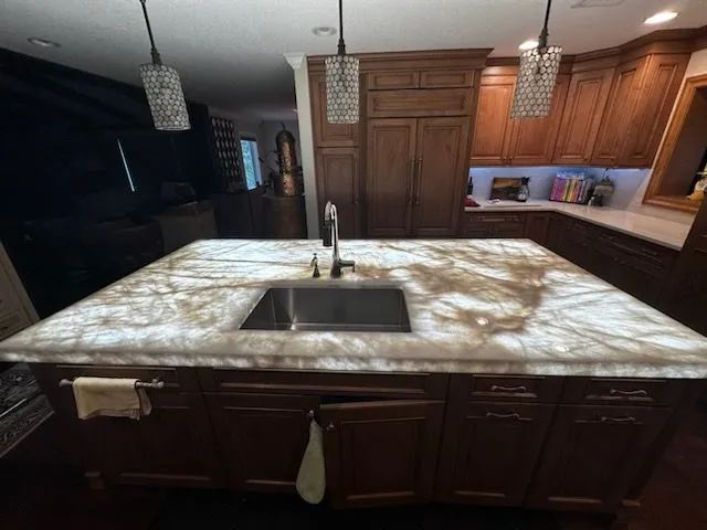 Modern kitchen with a large stone island, sink, wood cabinets, and pendant lights.
