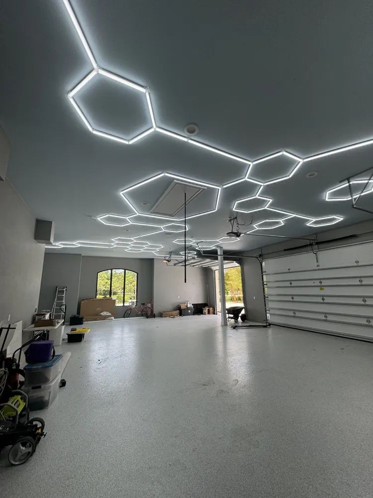 Modern garage interior with geometric LED ceiling lights, white floor, and a closed garage door