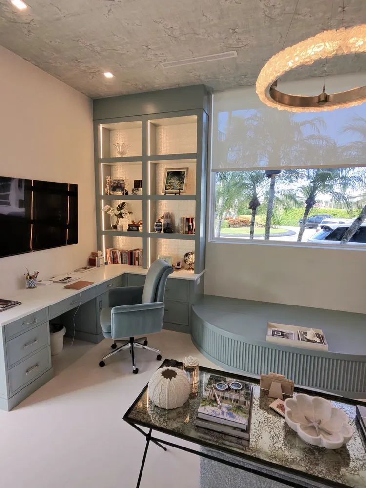 Modern home office with desk, swivel chair, built-in shelves, teal bench, and large window view