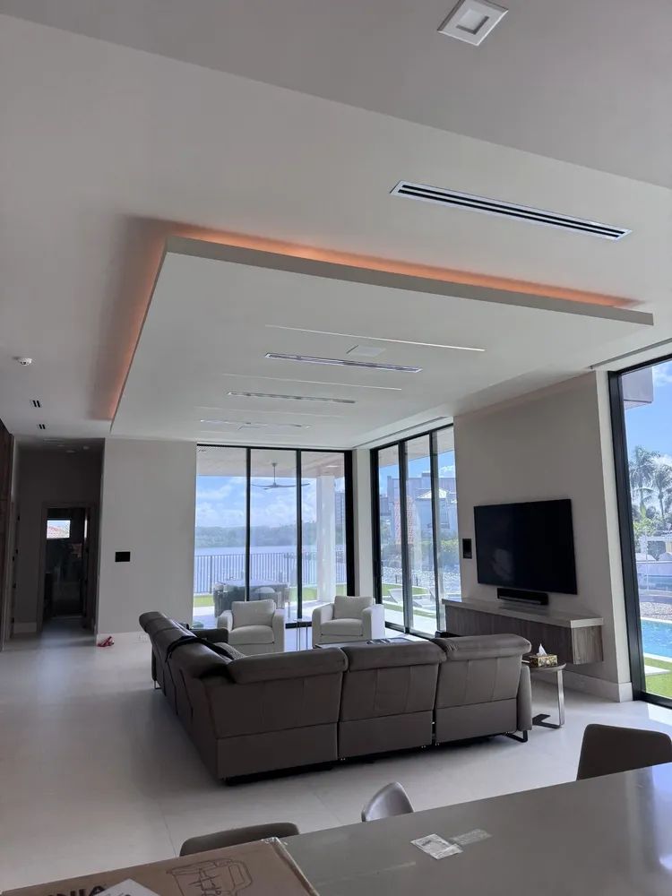 Modern living room with sectional sofa, wall-mounted TV, and floor-to-ceiling windows overlooking water and hills